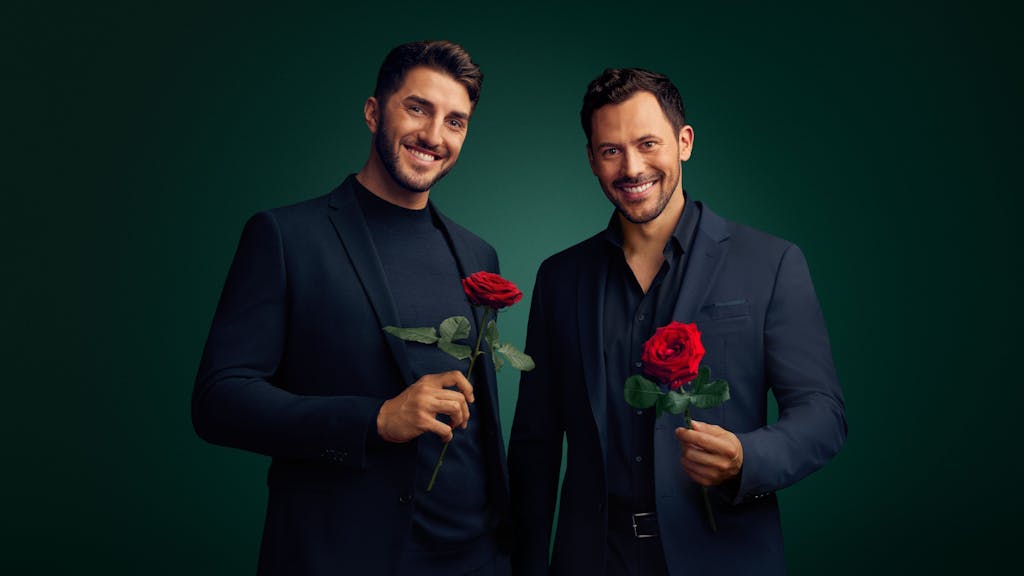 Dennis (l.) und Sebastian (r.) lächeln in die Kamera und halten einzelne Rosen in ihren Händen.