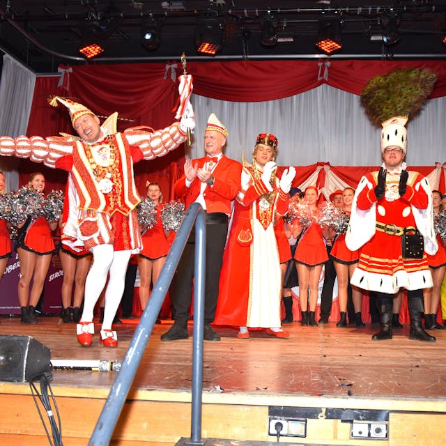 Ein Dreigestirn und eine Tanzgruppe stehen auf einer Bühne.