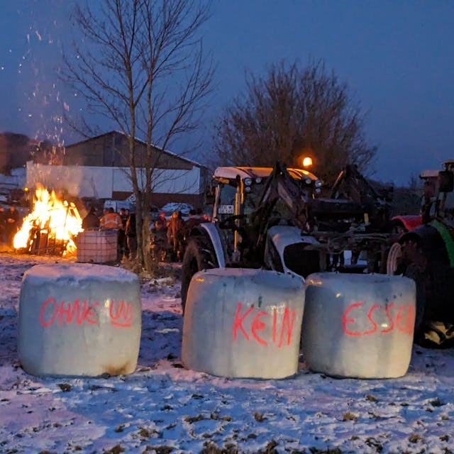 Ein Traktor und Strohballen mit Protest-Aufschriften stehen vor einem Feuer.&nbsp;