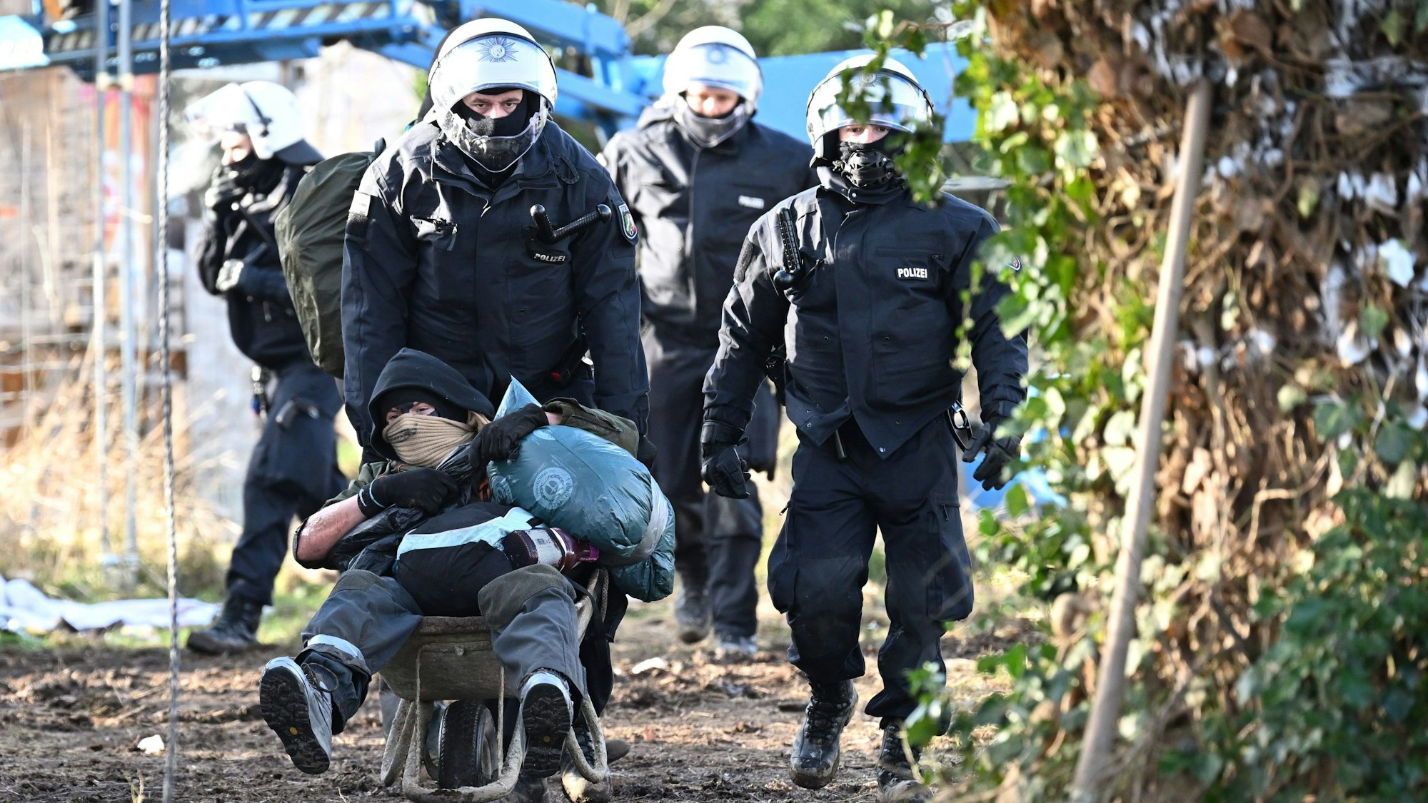 Erkelenz: Polizisten schieben einen Klimaaktivisten mit der Schubkarre vom Gelände in Lützerath.