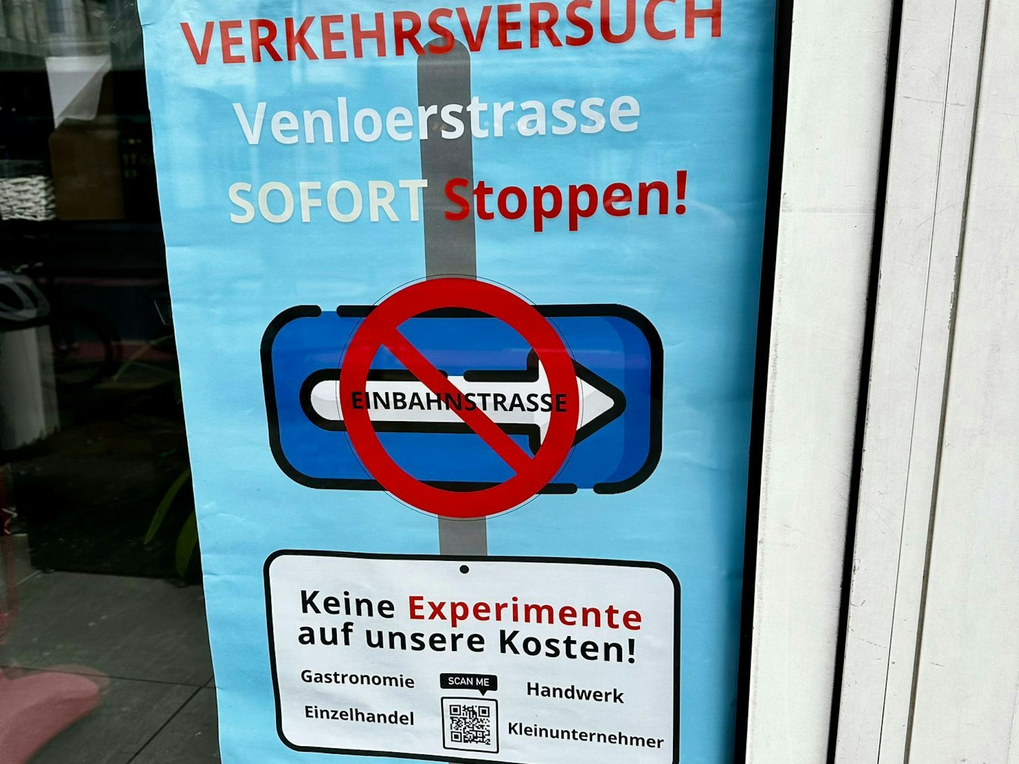 In einem Schaufenster ist das Plakat mit der Forderung Verkehrsversuch Venloer Straße sofort stoppen! zu sehen.