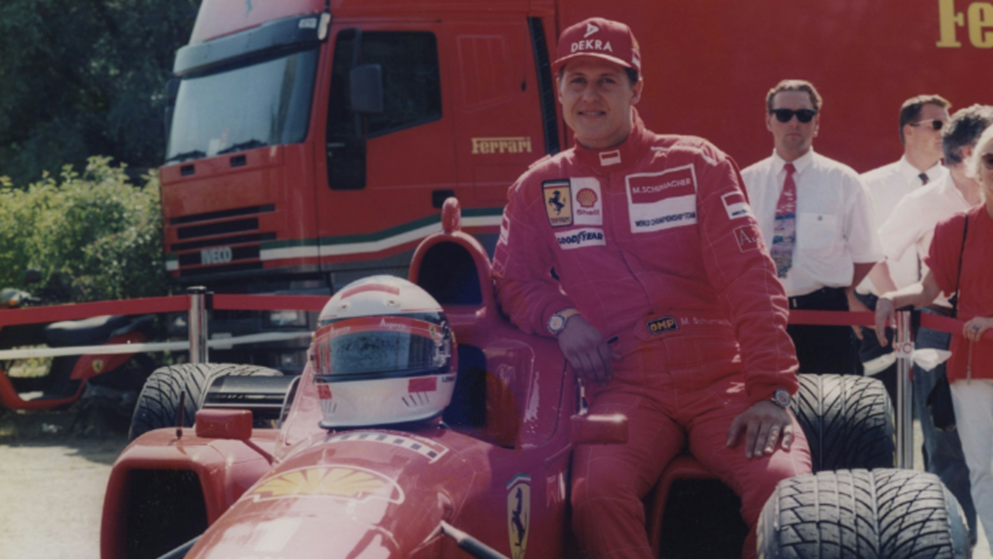 Zu sehen ist Rennfahrer Michael Schumacher, der sich an einen Ferrari lehnt.