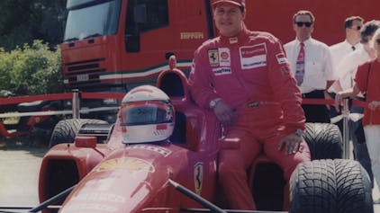 Zu sehen ist Rennfahrer Michael Schumacher, der sich an einen Ferrari lehnt.&nbsp;