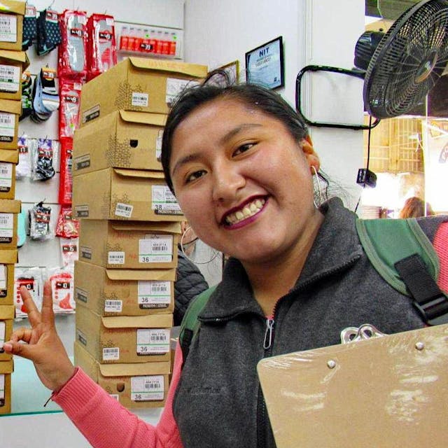 Ein junge Frau steht vor vielen Paketen und lacht in die Kamera.