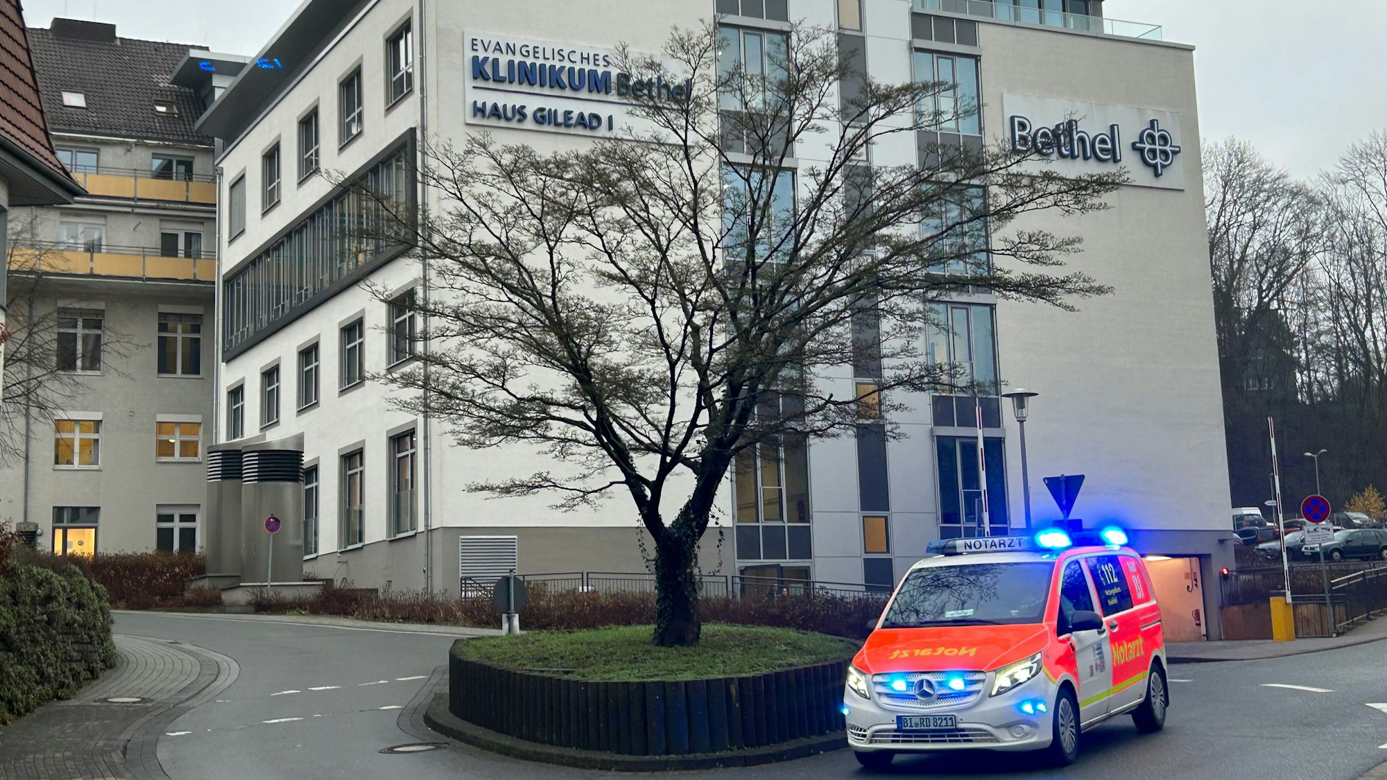 Blick auf das Gebäude des Klinikums Bethel in Bielefeld. Ein Rettungswagen mit Blaulicht fährt vorbei.