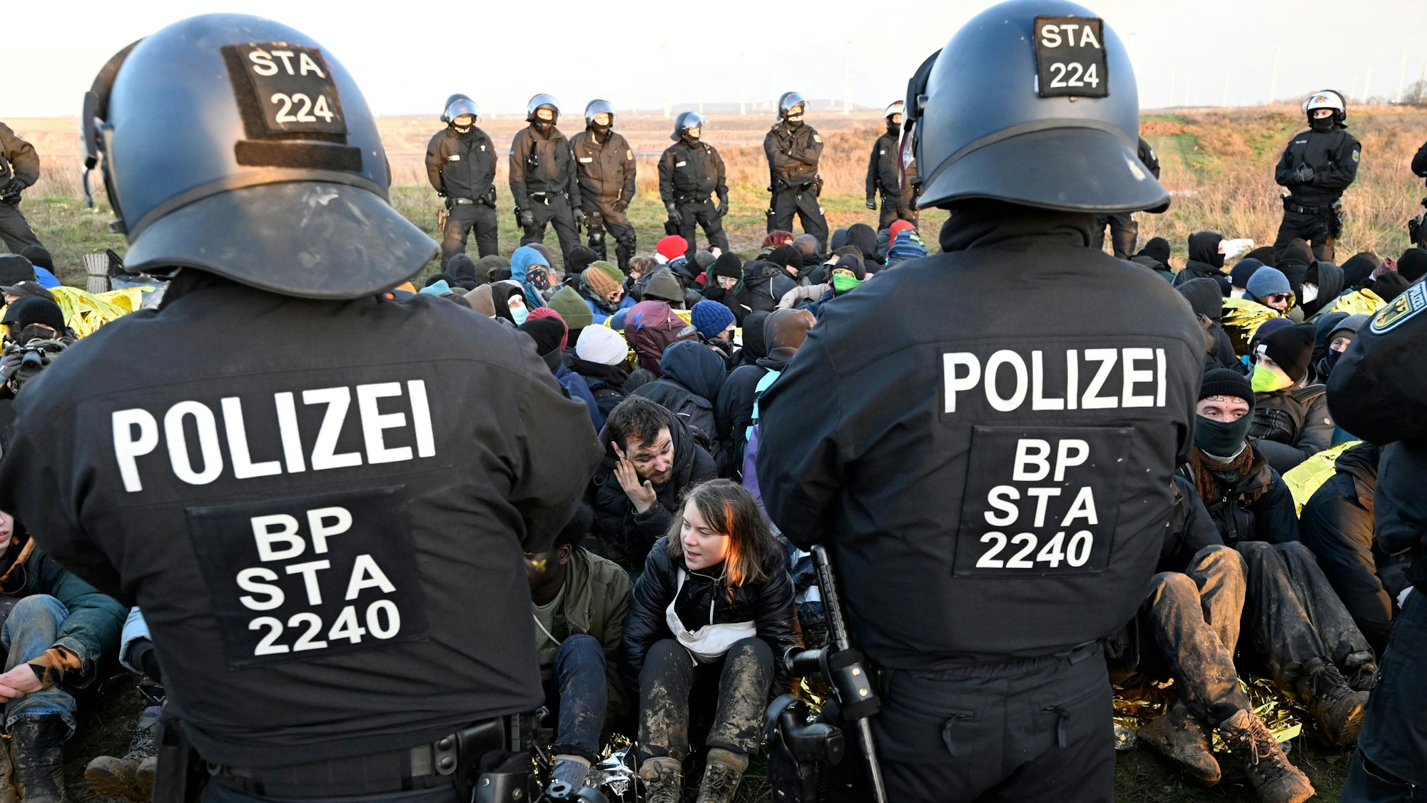 Polizisten stehen vor einer Gruppe von Demonstranten, darunter auch die die schwedische Klimaaktivistin Greta Thunberg (Mitte, unten), am Rand des Braunkohlentagebaus Garzweiler II bei einer Protestaktion von Klimaaktivisten nach der Räumung von Lützerath. Aktivisten und Kohle-Gegner setzen ihre Proteste am Dienstag an mehreren Orten in Nordrhein-Westfalen fort. +++ dpa-Bildfunk +++