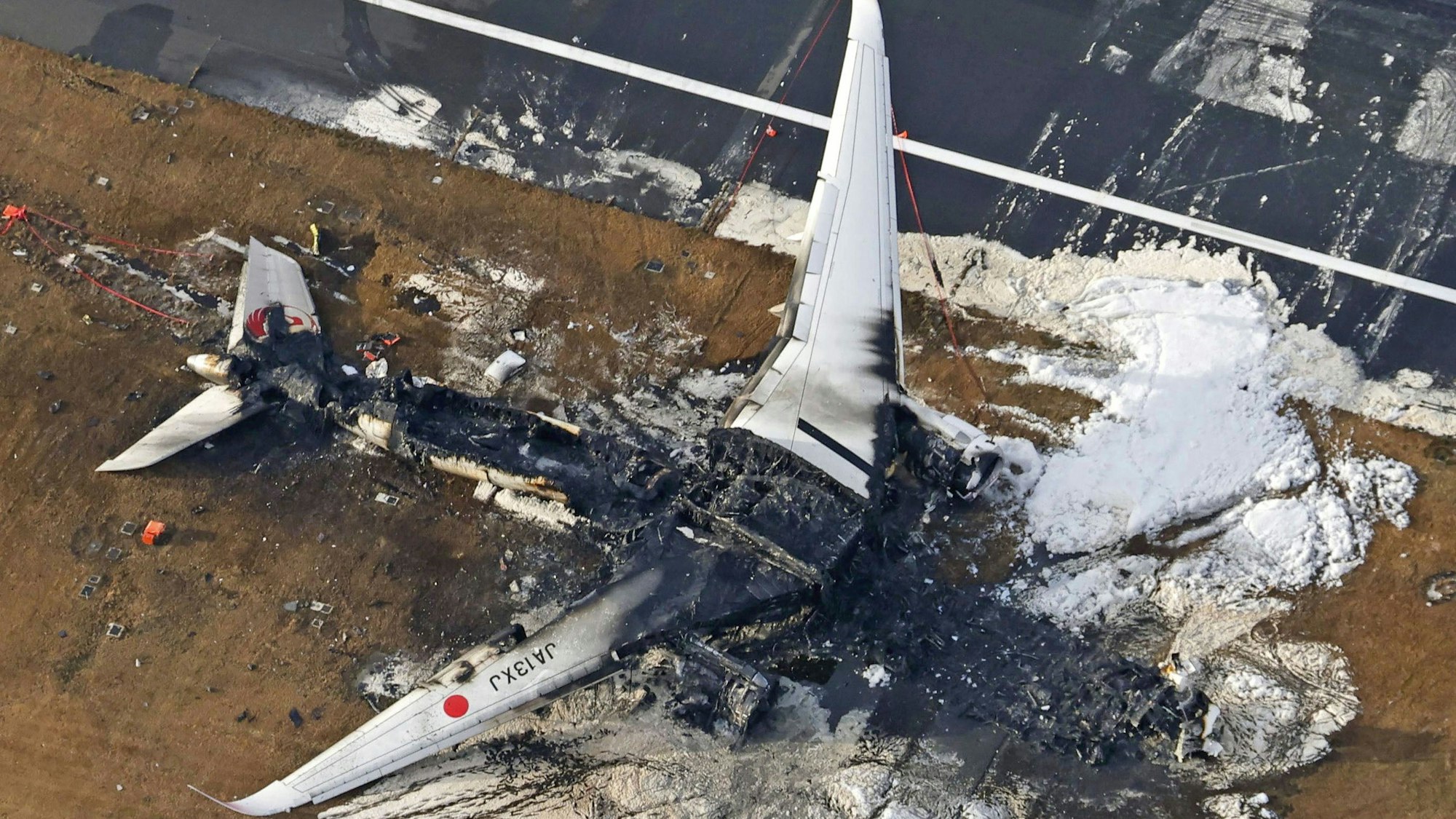 Der ausgebrannte Airbus A350 der japanischen Fluggesellschaft Japan Airlines kurz nach dem Zusammenstoß mit einer Bombardier DHC-8 der japanischen Küstenwache. Das Flugzeugwrack ist komplett verbrannt, nur noch Reste der Flügel sind zu erkennen.