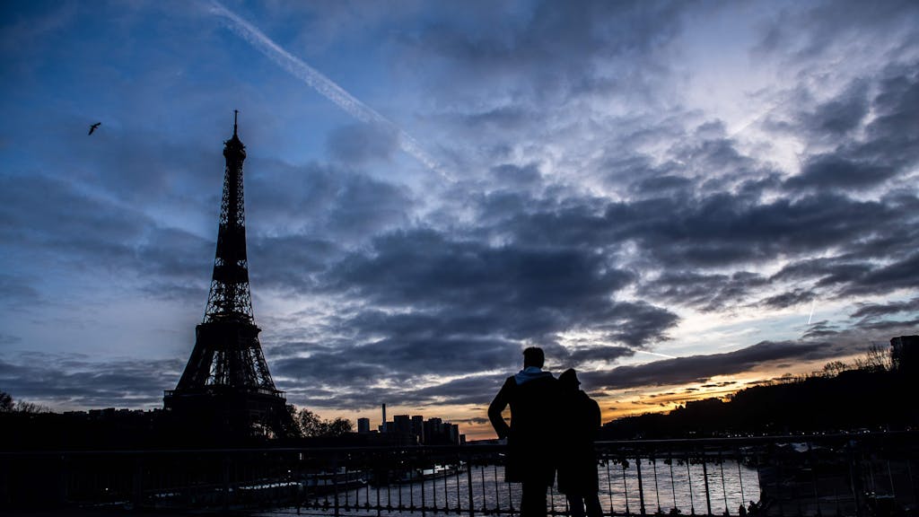 Ein Paar steht auf der Debilly-Fußgängerbrücke an der Seine und betrachtet den Sonnenuntergang hinter dem Eiffelturm.