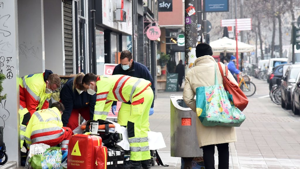 Rettungssanitäter und Notarzt kümmern sich um einen Obdachlosen an einem Straßenrand.