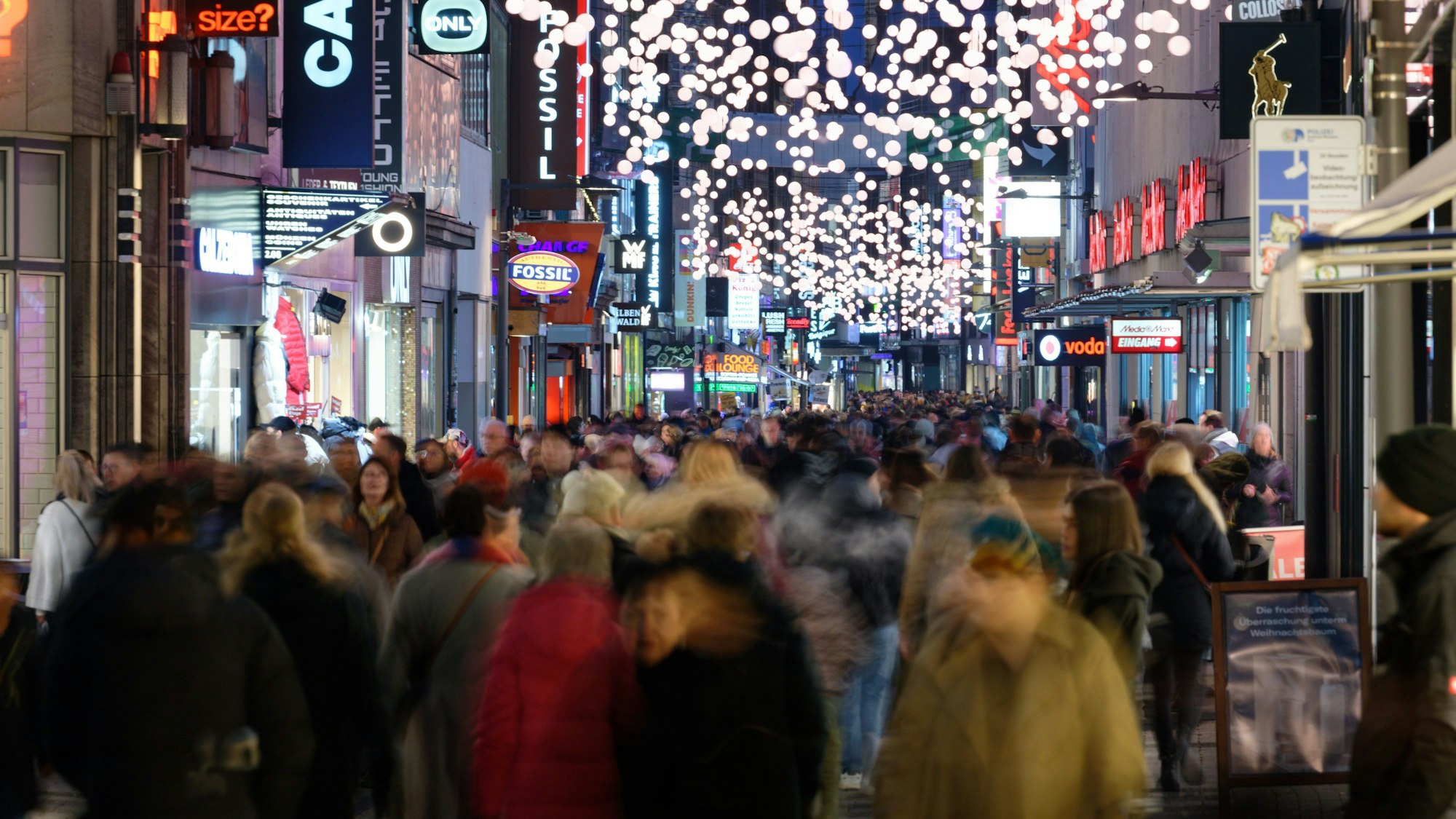 Einkäufer gehen durch eine mitWeihnachtslichtern geschmückte Einkaufsstraße
