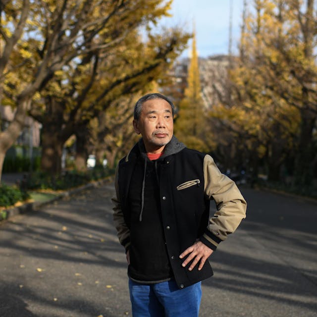 Porträt des Autors Haruki Murakami, der eine Collegejacke trägt und in einer Allee in Tokyo steht.