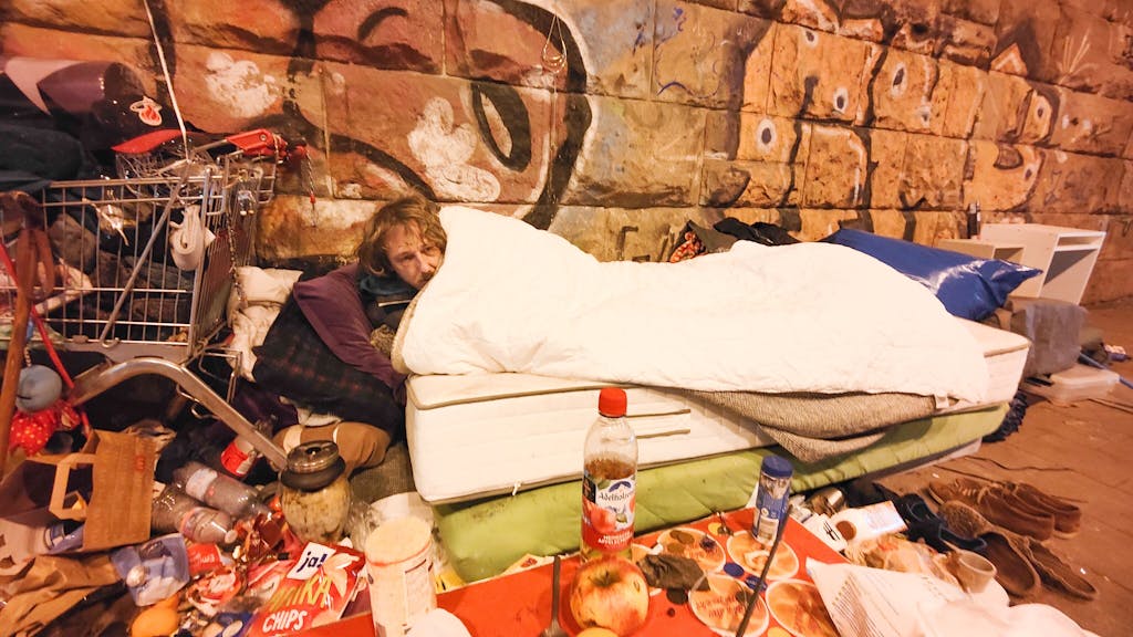 Ein Obdachloser liegt auf einer Matratze auf einer Straße.