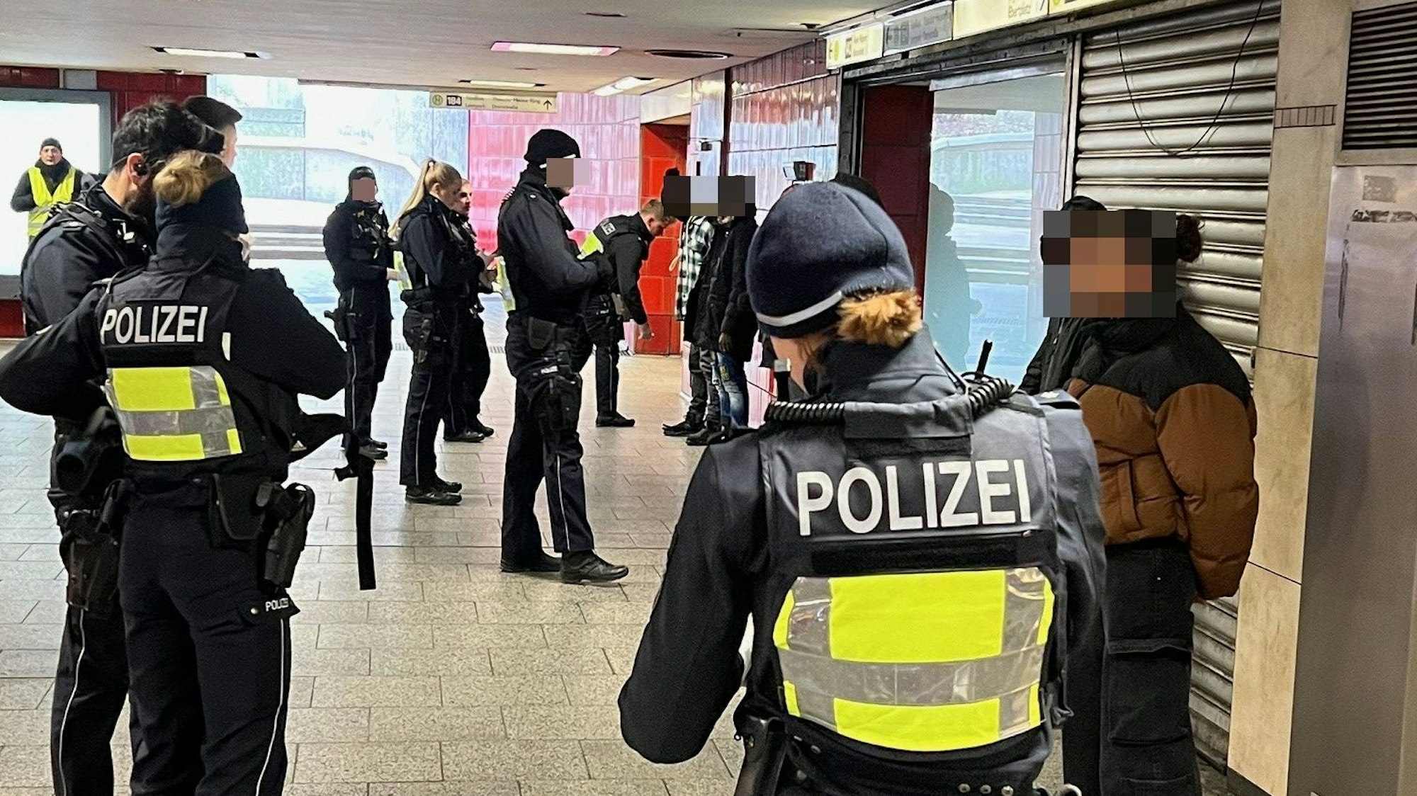 Polizisten durchsuchen mehrere mutmaßliche Drogendealer oder deren Kunden, die mit dem Rücken zu einer Wand in der KVB-Zwischenebene am Ebertplatz stehen.