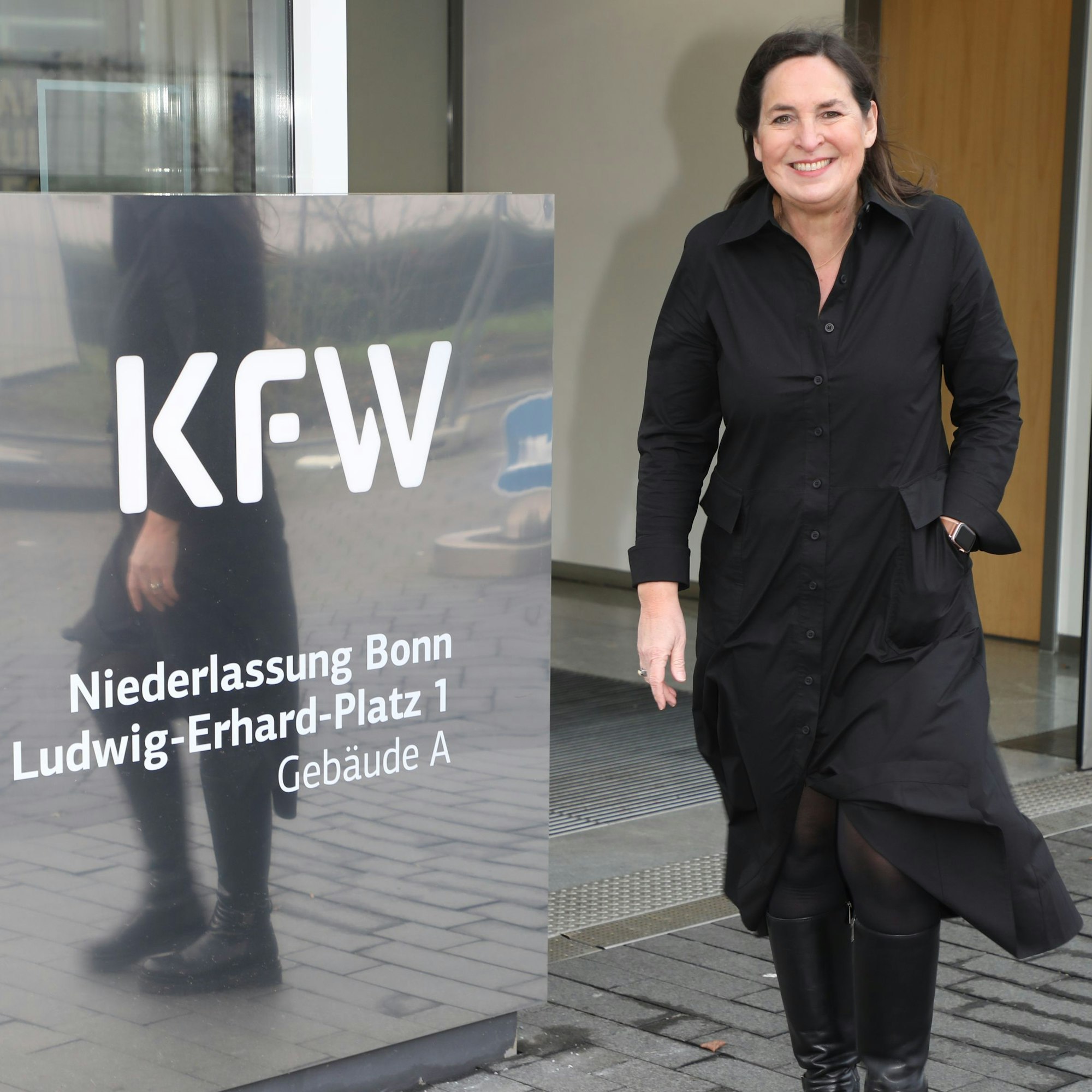 Jungfrau Sabine (Auweiler) geht an einem Schild mit der Aufschrift „KfW“ vorbei.