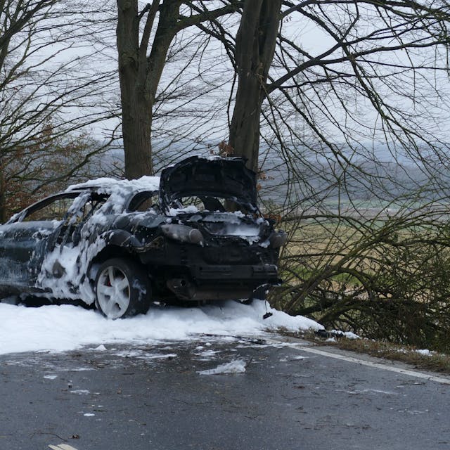 Ein ausgebranntes Auto steht mit Löschschaum bedeckt auf einer Straße.