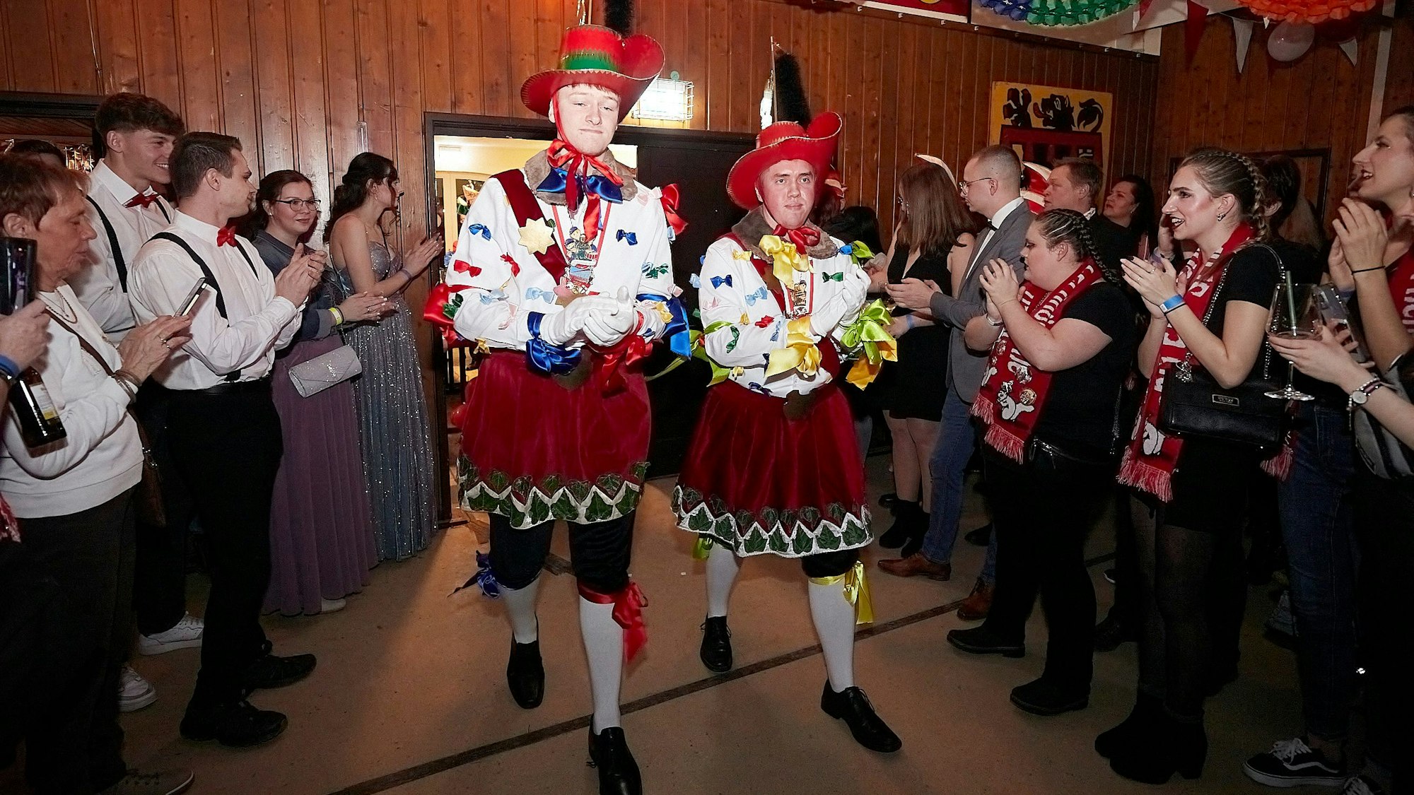 Tom Franzen und Noel Mercier als Jecke Böhnchen betreten den Saal, empfangen von einem Spalier klatschender Karnevalistinnen und Karnevalisten.