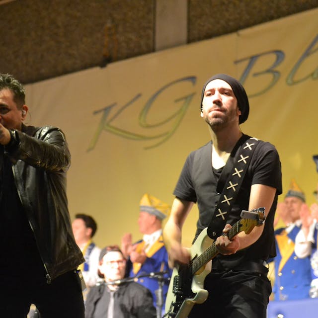 Der Sänger der Gruppe Domstürmer, Micky Nauber, auf der Karnevalsbühne in Weilerswist, neben ihm ein Gitarrist der Band, im Hintergrund Mitglieder des Elferrats.