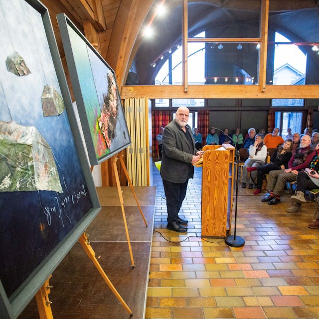 Künstler Uwe Appold hält einen Vortrag. Hinter ihm stehen mehreren Bilder.