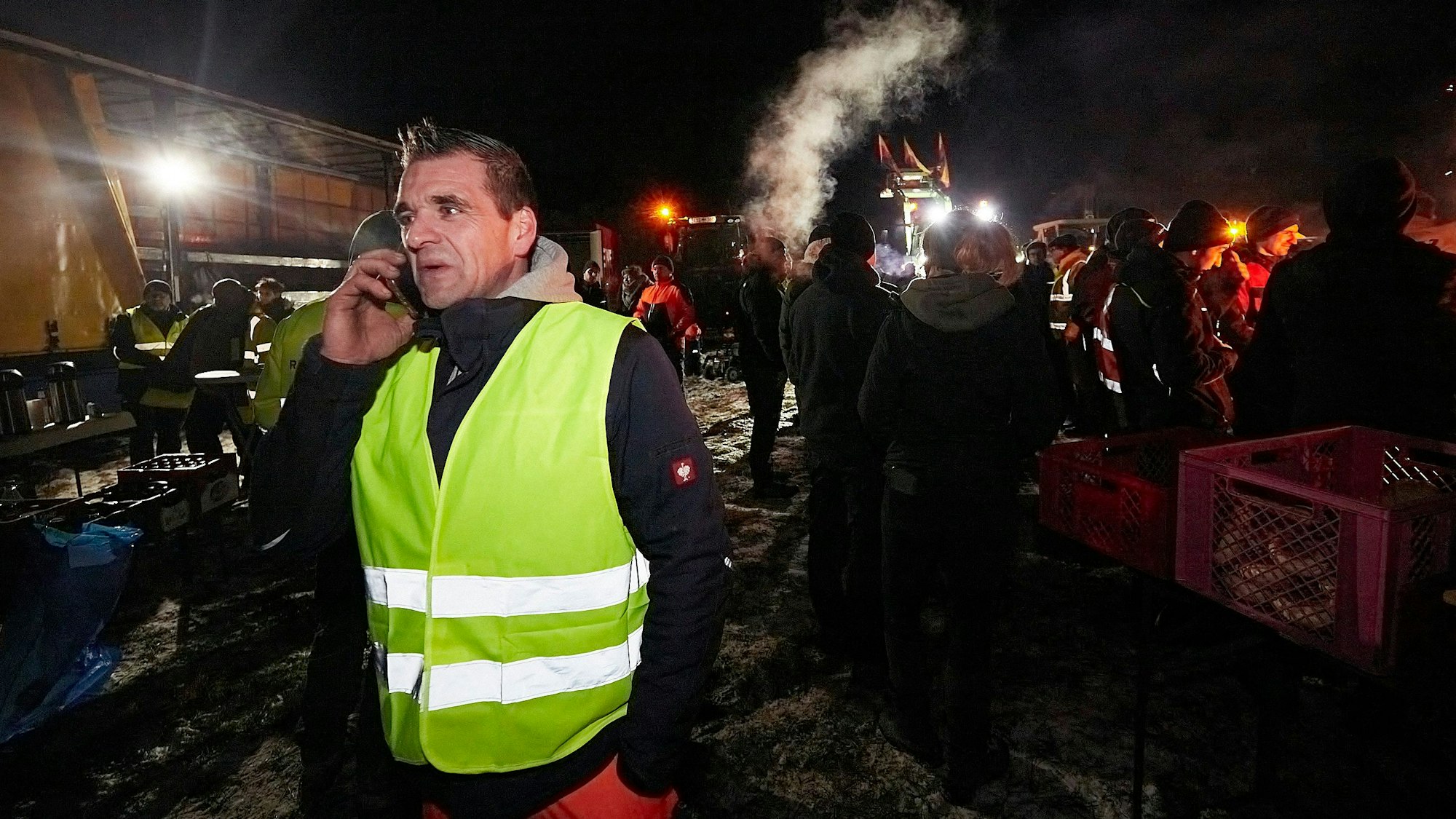 Dieter Michels trägt eine gelbe Warnweste. Er steht am Rande des Mahnfeuers und telefoniert mit dem Handy.