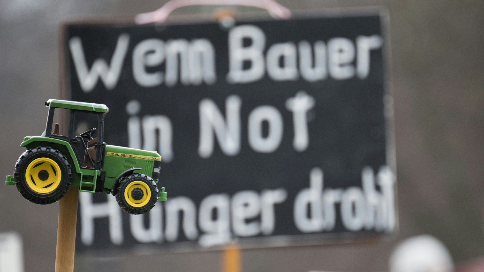 „Wenn Bauer in Not Hunger droht“ steht während einer Demonstration in Berlin auf einem Plakat, davor ist ein Spielzeugtraktor zu sehen.