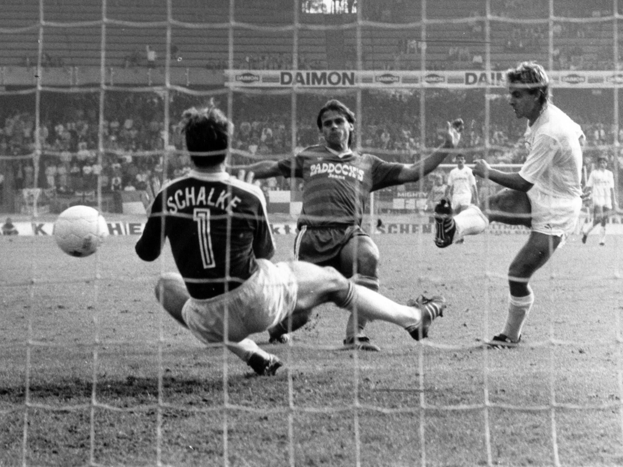 Pierre Littbarski (r., 1. FC Köln) trifft gegen Olaf Thon (m.) und Torwart Walter Junghans (Schalke) zum 3:2 im Spiel gegen FC Schalke (1985).