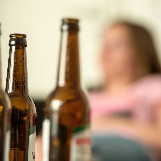 Ein Frau sitzt hinter leeren Bierflaschen.&nbsp;