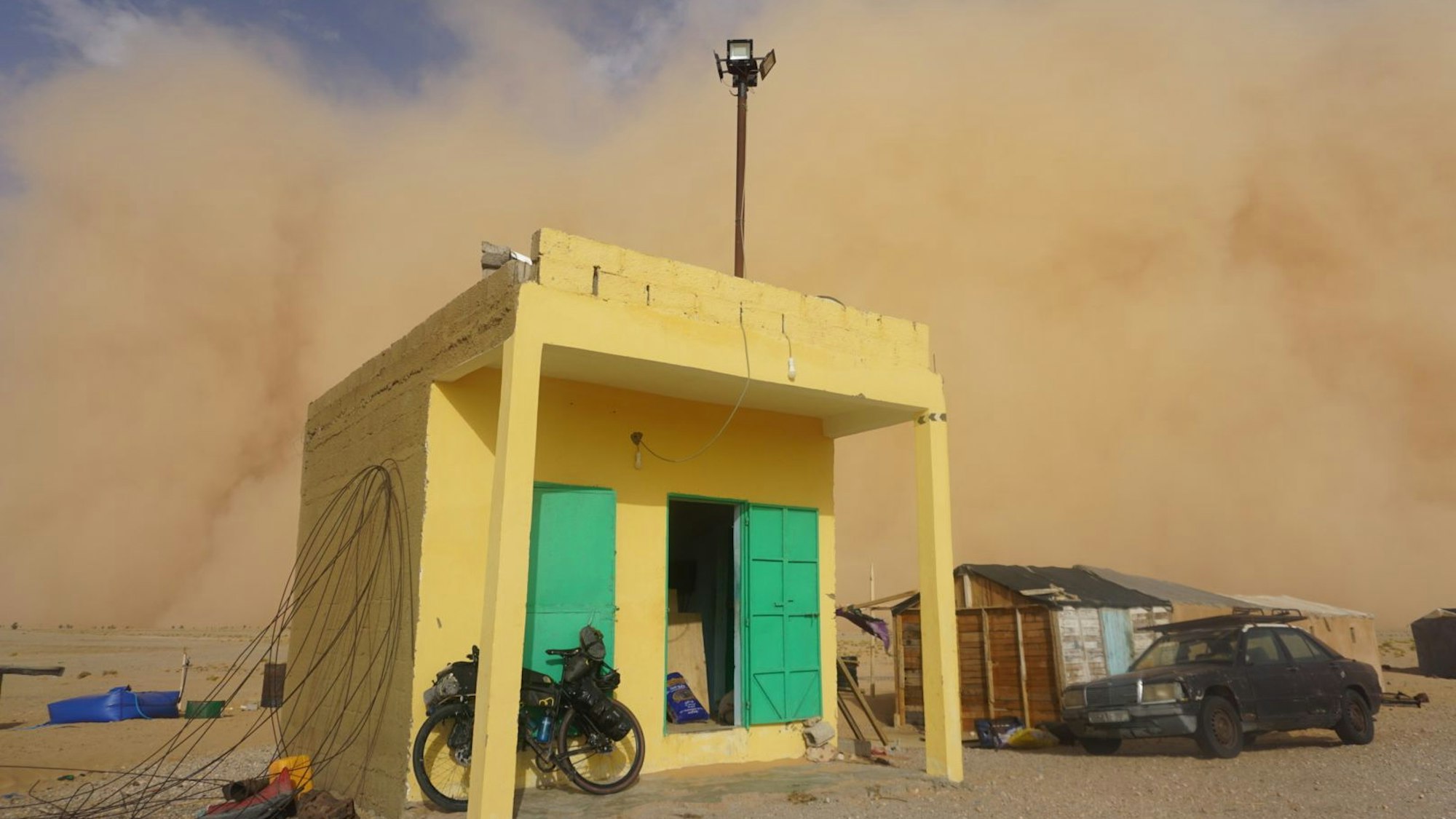 Ein kleines Gebäude am Straßenrand, dahinter ist der Sandsturm zu sehen.