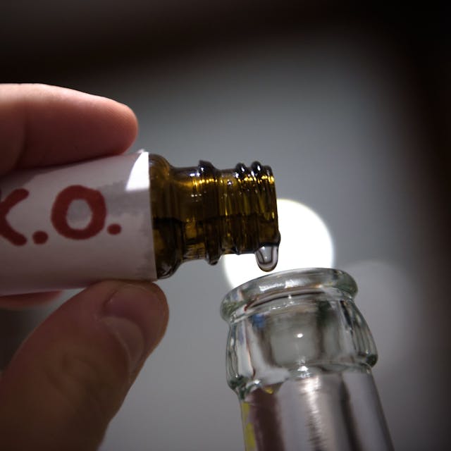Aus einem Fläschchen mit der Aufschrift „K.O.“ wird eine klare Flüssigkeit in eine Glasflasche geträufelt.