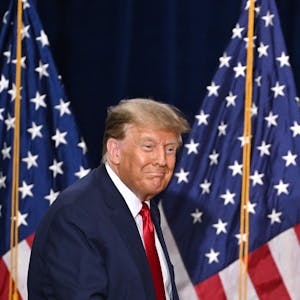 Ex-US-Präsident Donald Trump steht auf einer Bühne vor zwei Flaggen der Vereinigten Staaten und blickt lächelnd ins Publikum.