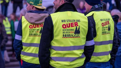Drei Männer in gelben Warnwesten mit der Aufschrift „Wir stellen uns quer. Kein Rassismus bei uns in Köln“
