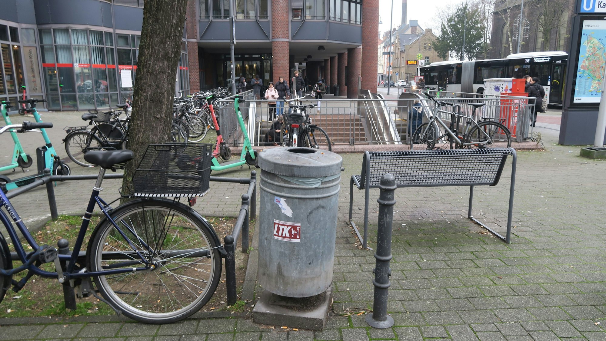 Ein öffentlicher Abfallbehälter steht an einem kleinen Platz an einem Eingang zur U-Bahn.