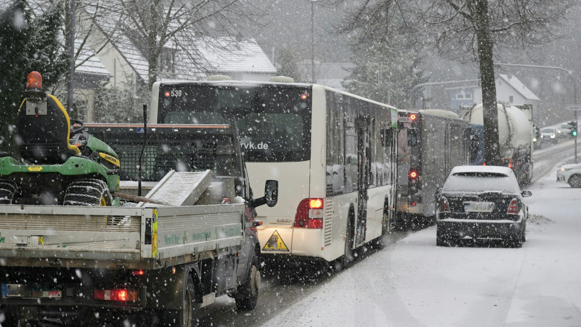 Busse, Lkw und Autos fahren auf einer Straße durchs Schneetreiben.