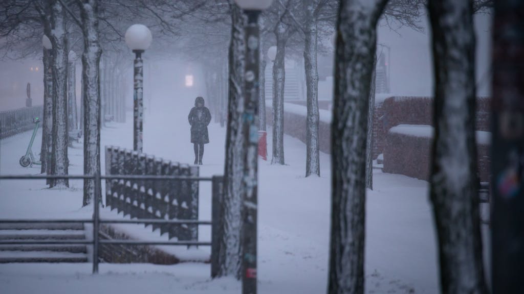Eine Fußgängerin ist am Morgen im Schneetreiben unterwegs. Der Winter ist zurück in Deutschland.