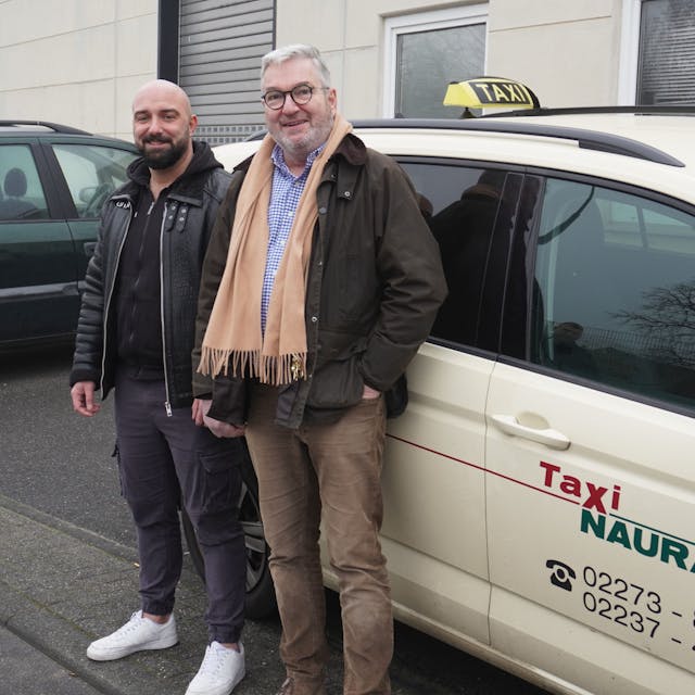 Kerim Kasikci und Thomas Naurath stehen vor einem Taxi.