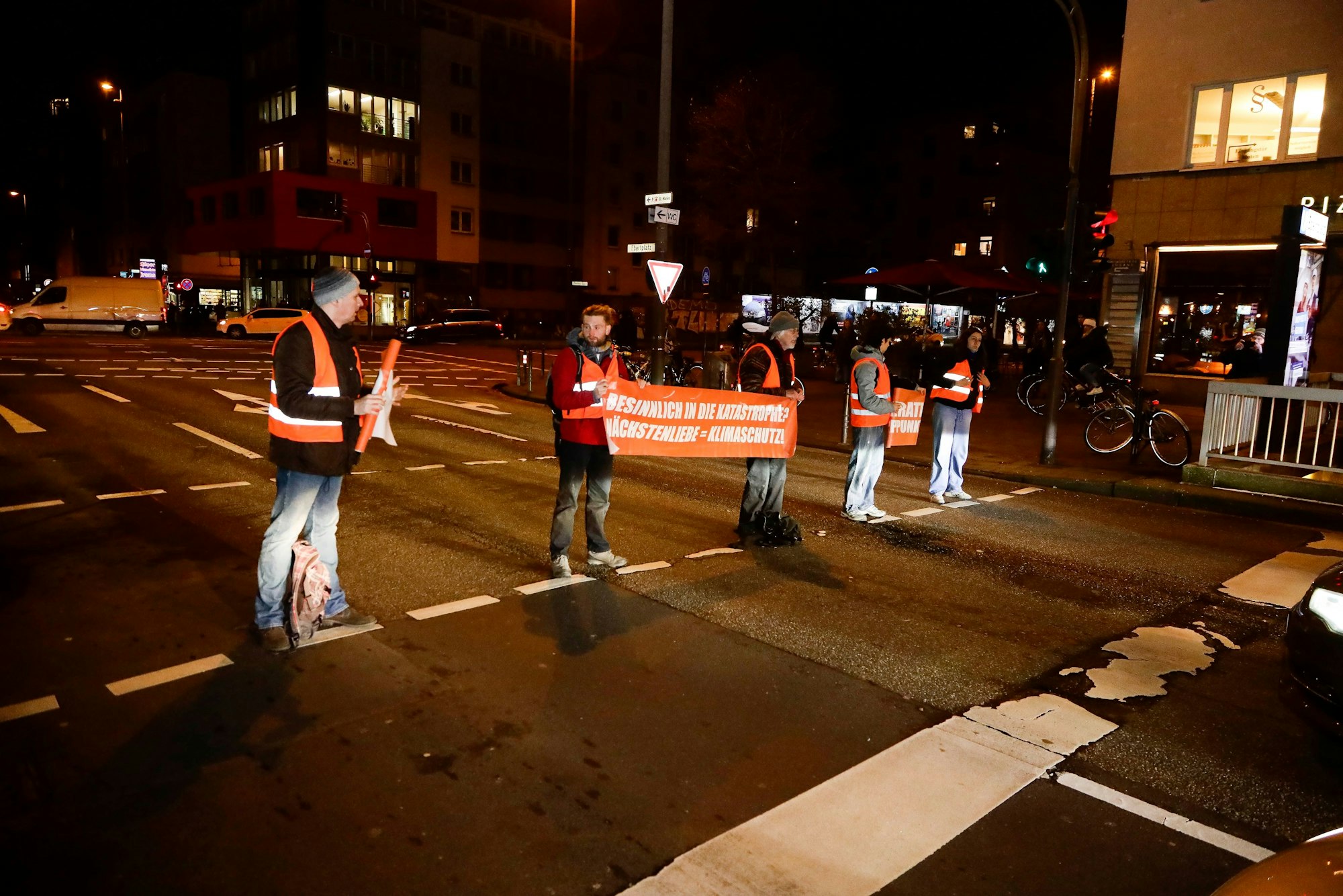 Aktivisten der Letzten Generation stehen auf einer Straße und halten ein Plakat in der Hand.