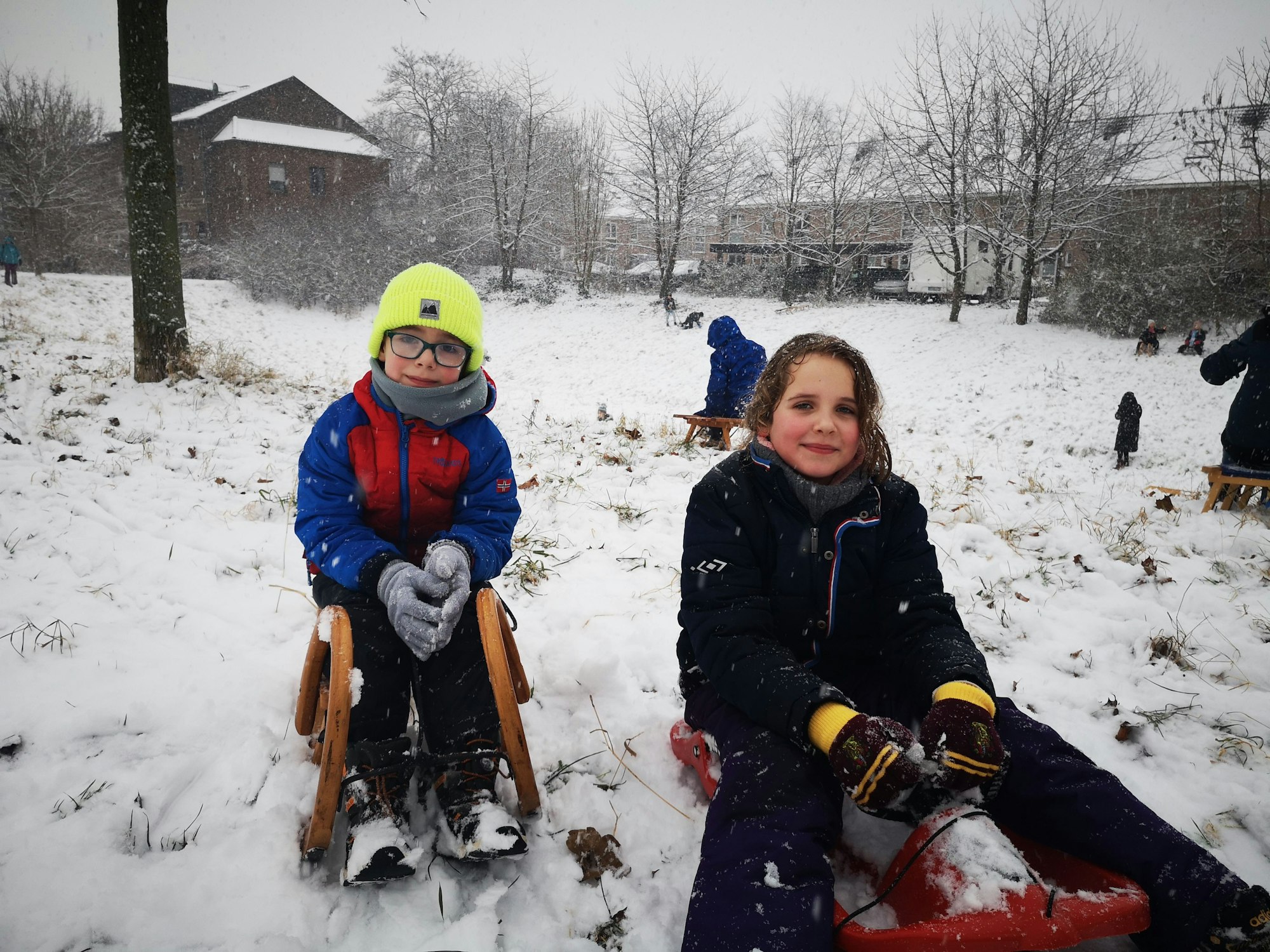 Ein Junge und ein Mädchen sitzen in dicke Winterkleidung gehüllt auf ihren Schlitten.