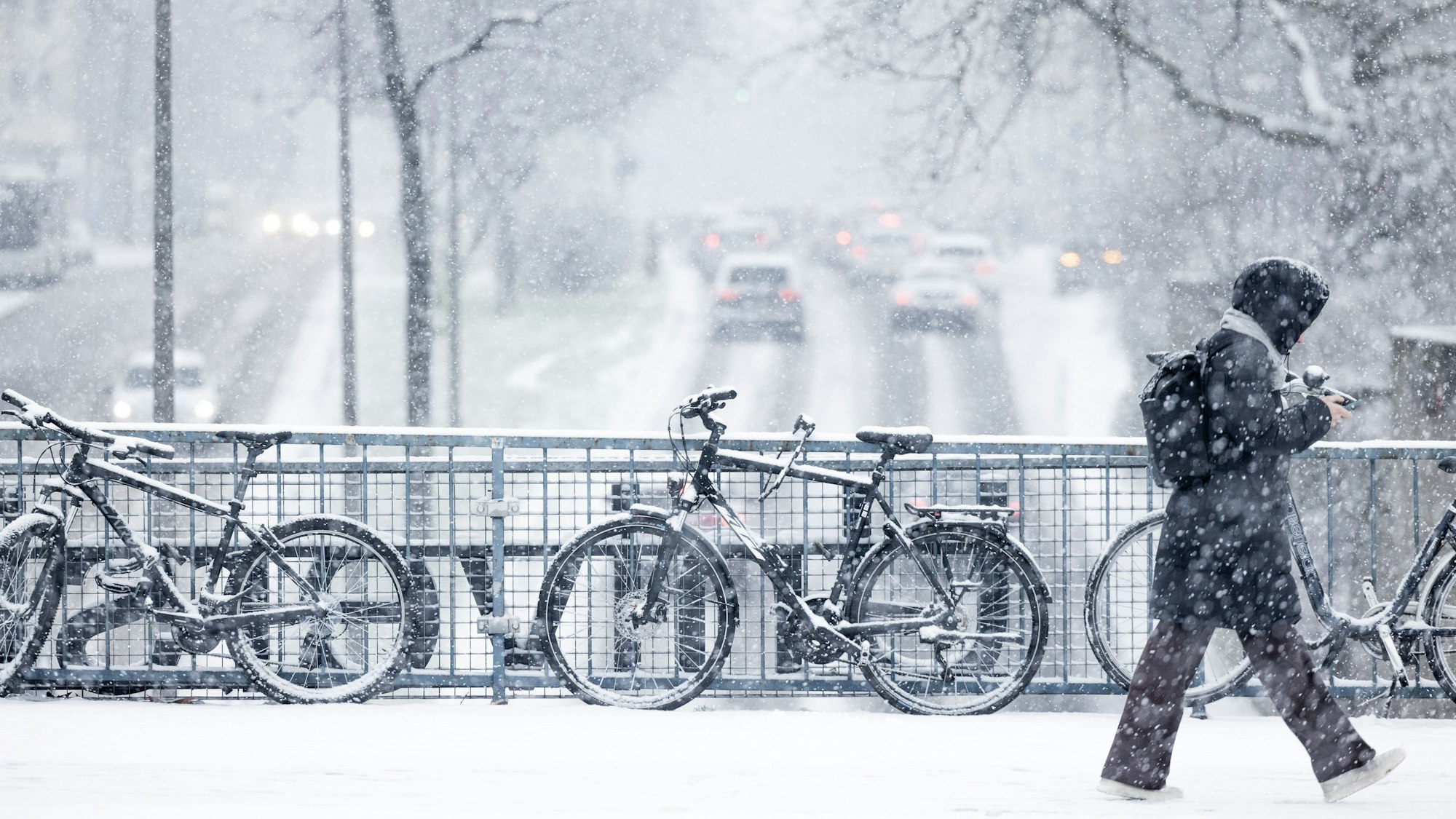 Schneebedeckte Fahrräder stehen im dichten Schneetreiben auf der Brücke an der Universitätsstraße.