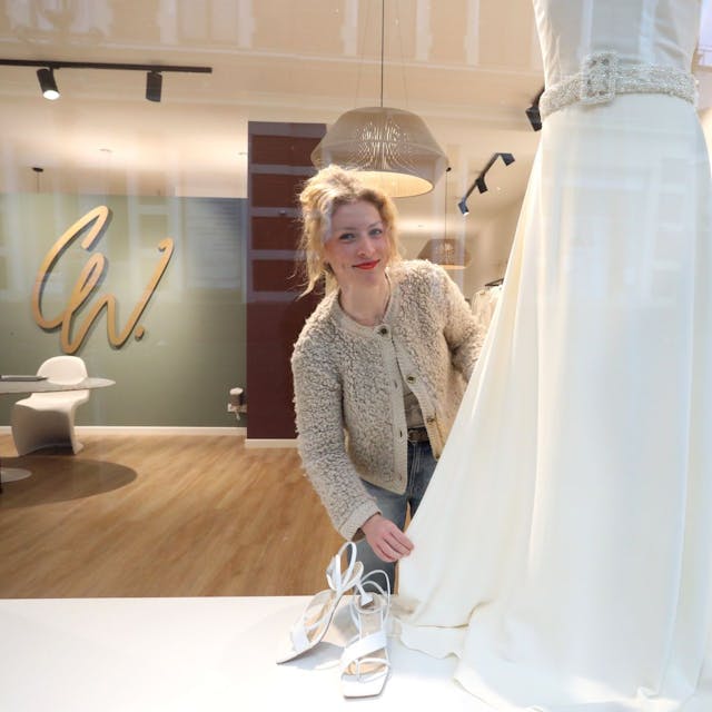 Eine Frau drapiert im Schaufenster ihres Brautmodengeschäfts ein weißes Hochzeitskleid.