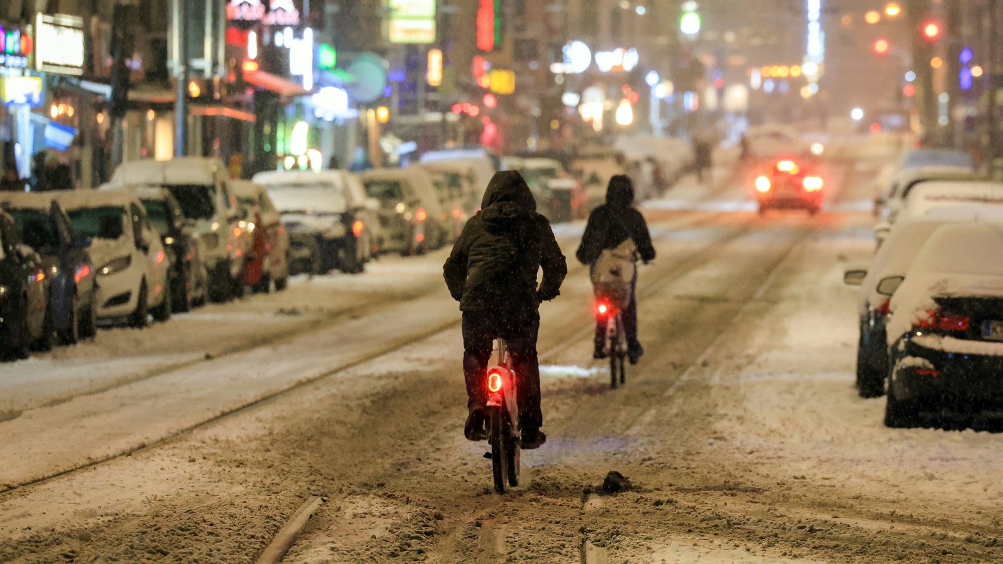 Fahrradfahrer von hinten auf einer verschneiten Straße mit Bahnschienen