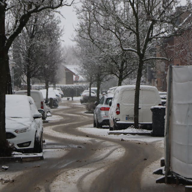 Eine verschneite Straße mit deutlichen Reifenspuren.