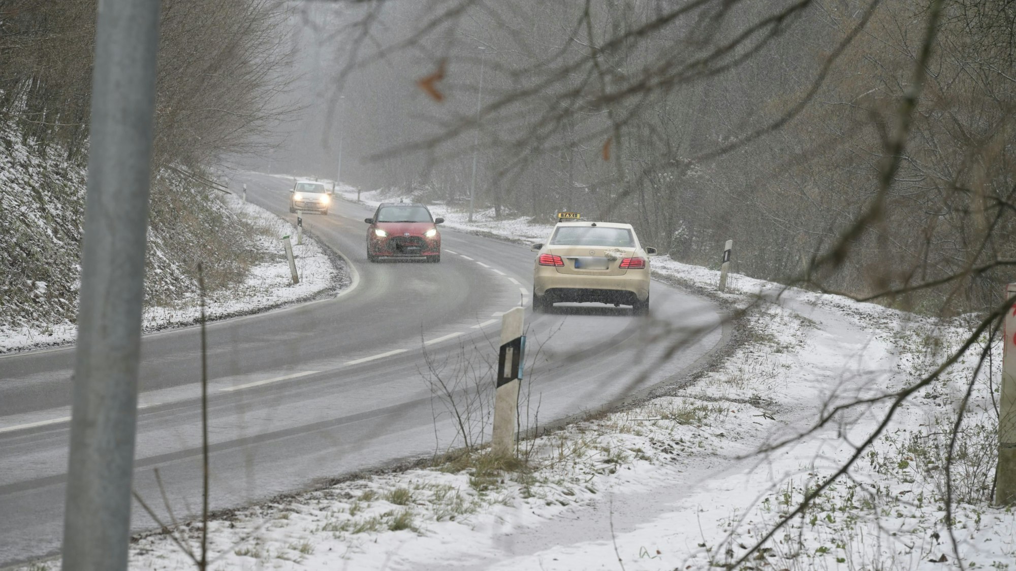 Autos fahren auf einer Straße durch eine verschneite Landschaft.