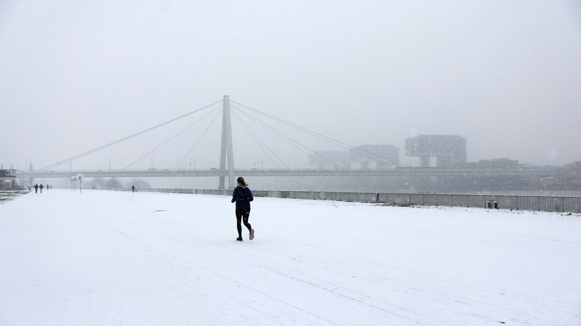 Eine Frau läuft über die schneebedeckte Straße am Rhein.