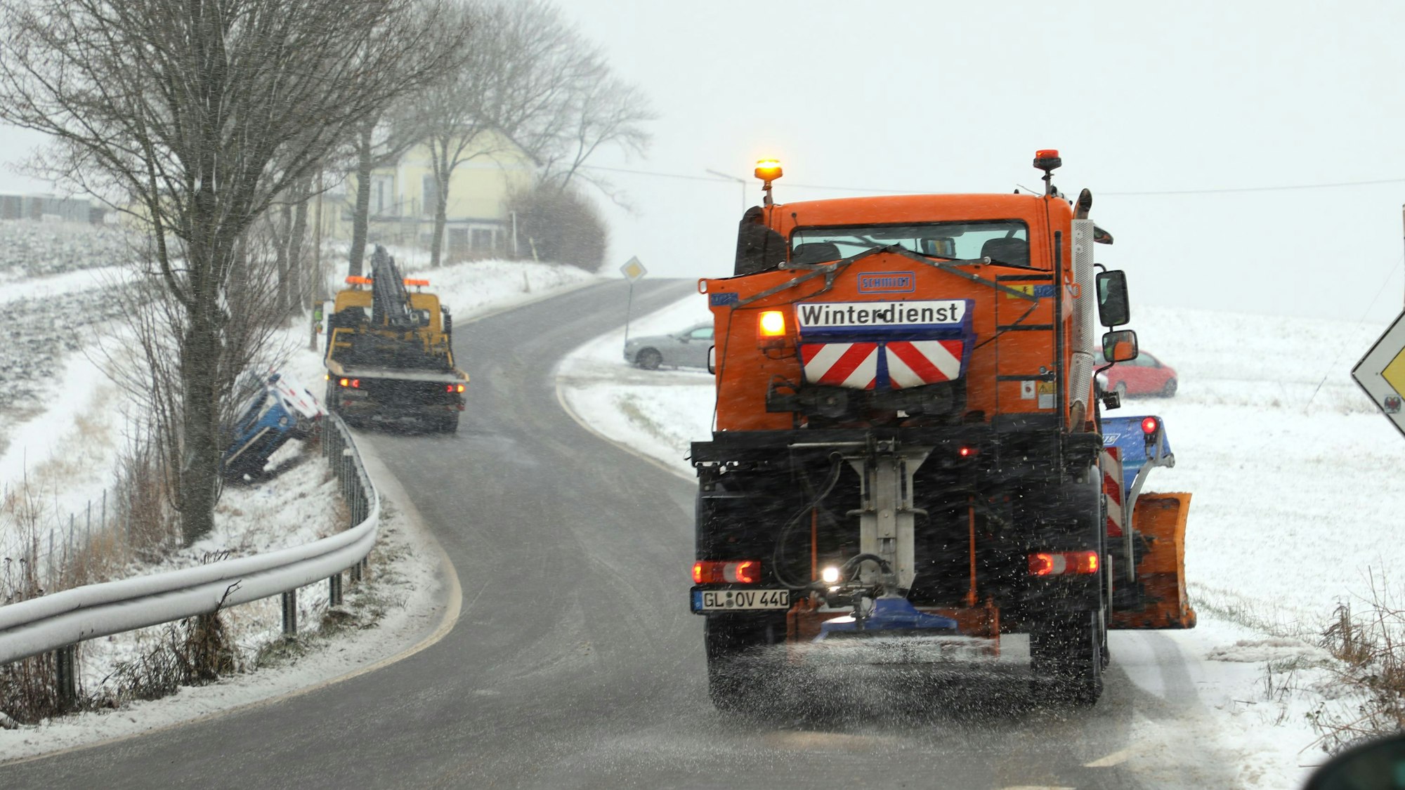 Ein Räumfahrzeug des Winterdienstes befreit eine Straße in der Eifel von Schneemassen. Weitere Schneeflocken fallen vom Himmel. (Symbolbild)