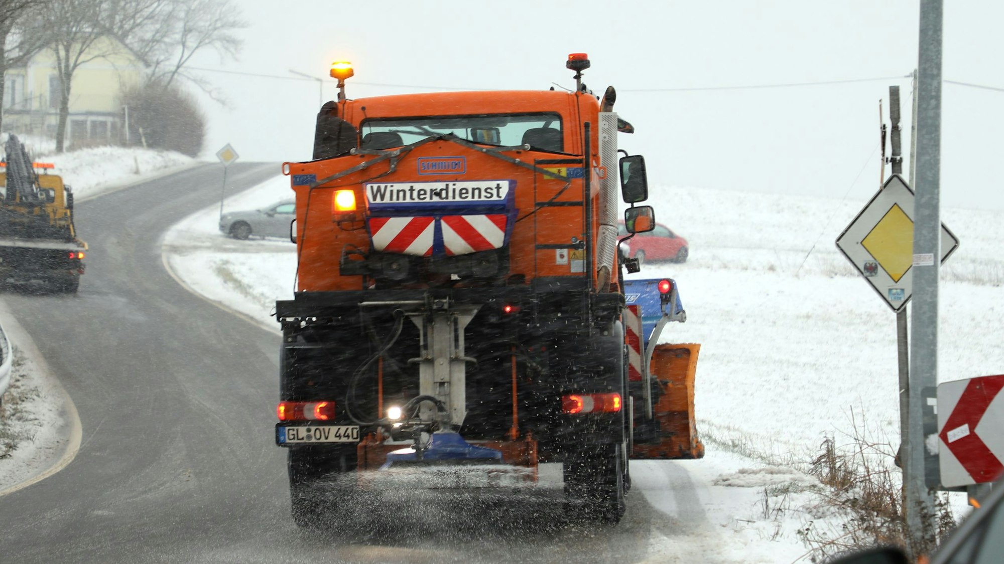 Ein Winterdienstfahrzeug mit Schneeräumschild und Salzstreuer fährt über eine Straße bei Overath-Kreutzhäuschen.
