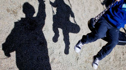 Zu sehen ist ein Kind auf einer Schaukel und sein Schatten, daneben ein weiterer Schatten eines Erwachsenen.
