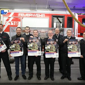 Eine Gruppe von acht Männern steht vor einem Feuerwehrfahrzeug. Sie halten Plakate in die Kamera.