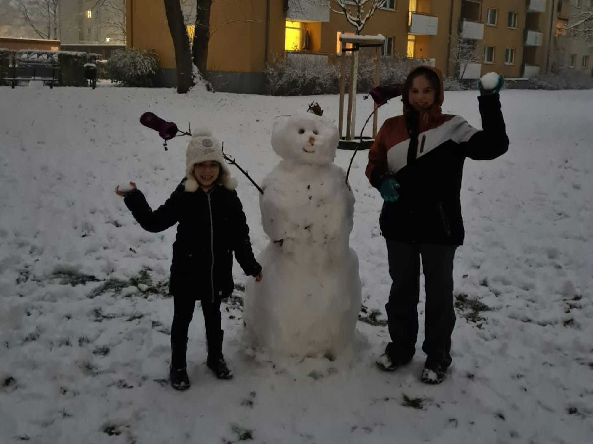 Zwei Kinder stehen neben einem Schneemann.