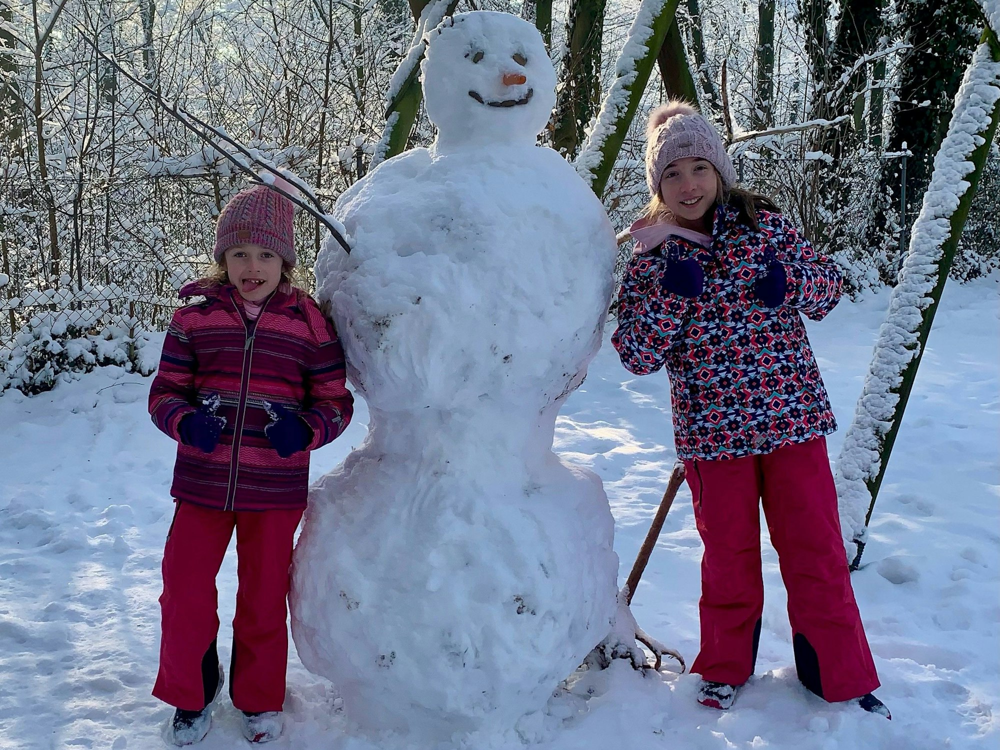 Zwei Mädchen stehen neben einem Schneemann.