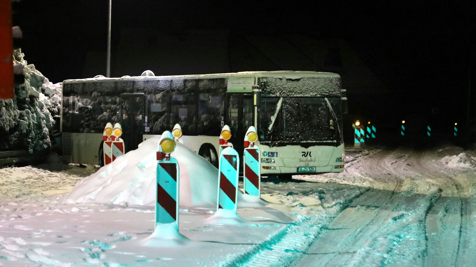 Ein Bus steht neben Warnbaken an einer verschneiten Straße.