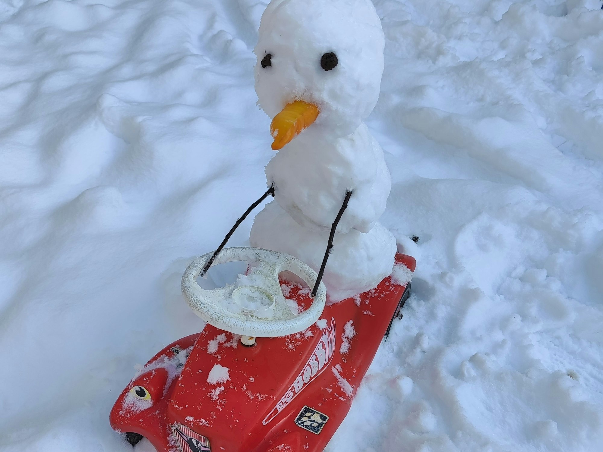 Ein kleiner Schneemann sitzt auf einem Bobbycar.